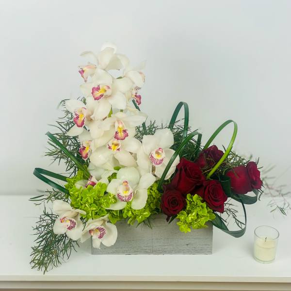 White orchids and red roses arranged in a rectangular box with a small candle beside it.