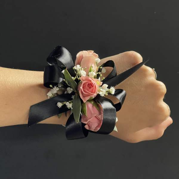 Pink rose wrist corsage with black ribbon on a hand
