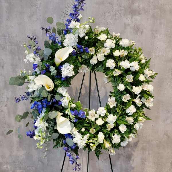 Large floral wreath with white calla lilies and blue flowers on a stand