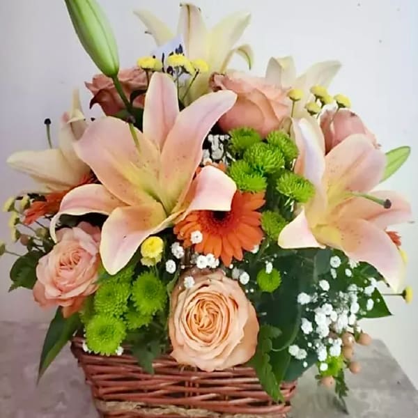 Basket arrangement of pink lilies, roses, and an orange gerbera daisy