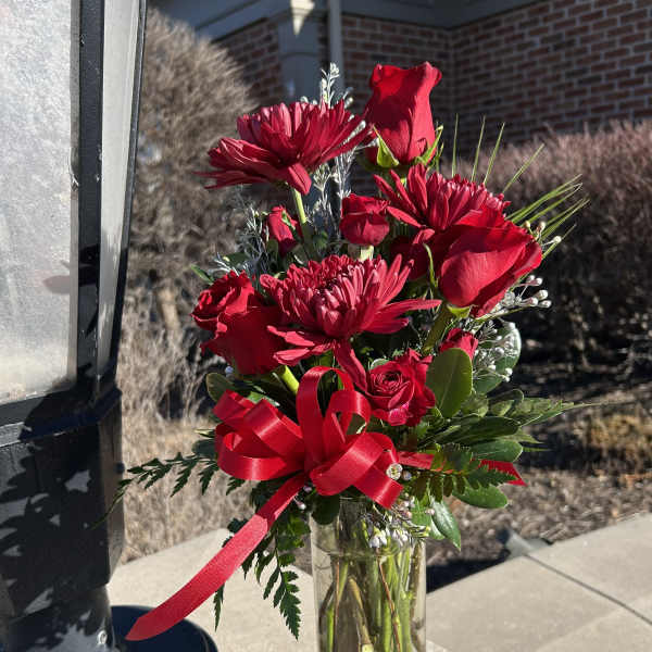 Red roses and chrysanthemums in a clear glass vase with a red ribbon