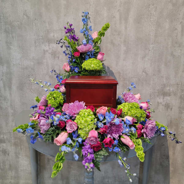 Colorful floral arrangement surrounding a wooden urn on a table