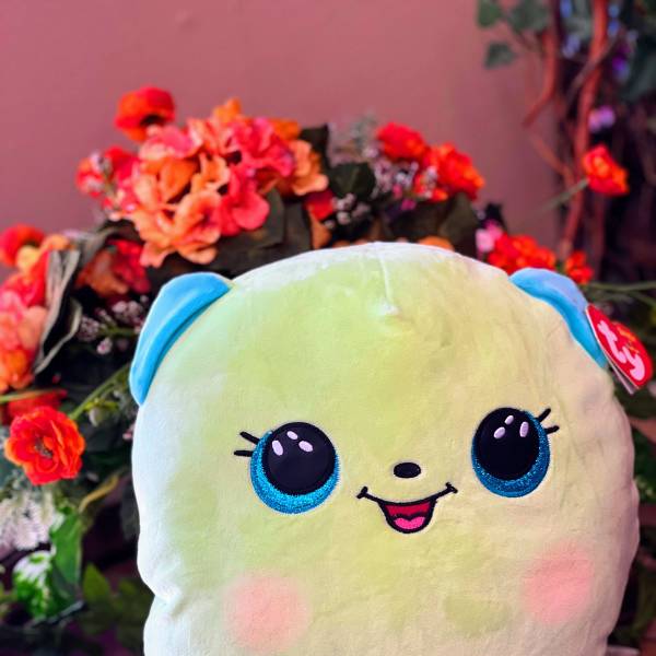 Plush smiling character pillow in front of orange flowers