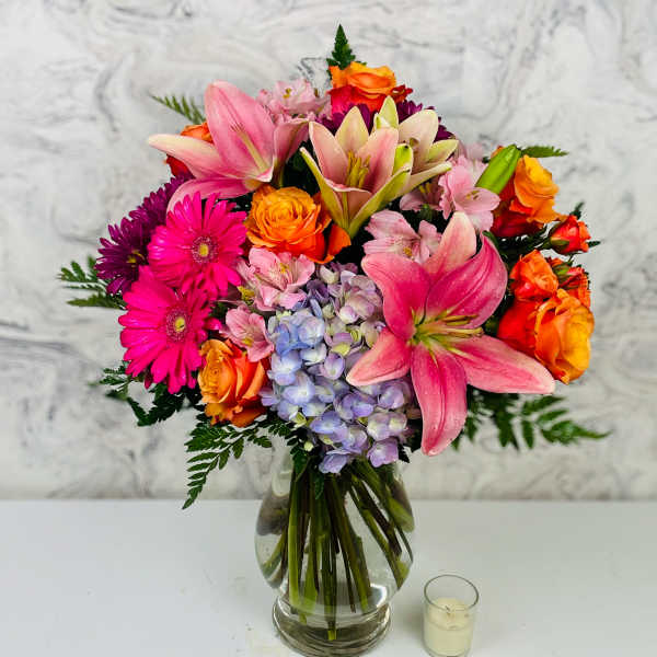 Mixed bouquet of pink lilies, orange roses, and purple flowers in a glass vase