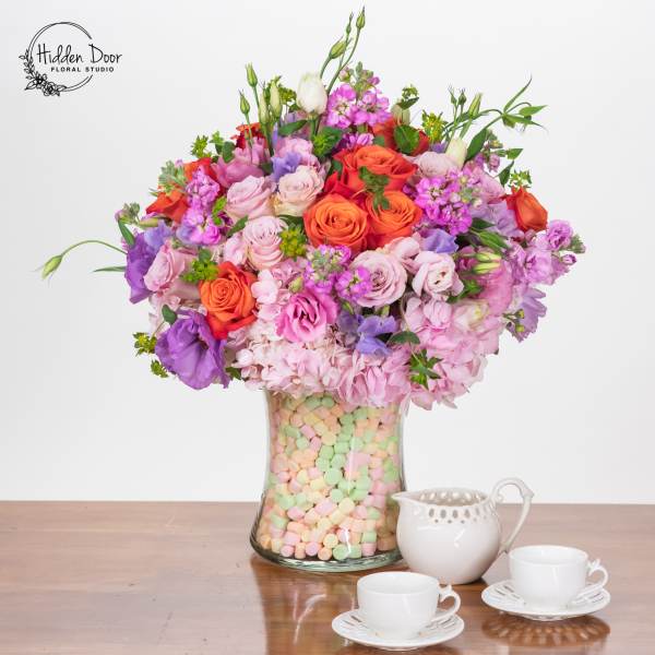 Mixed pink, purple, and orange flowers in a glass vase filled with pastel candies