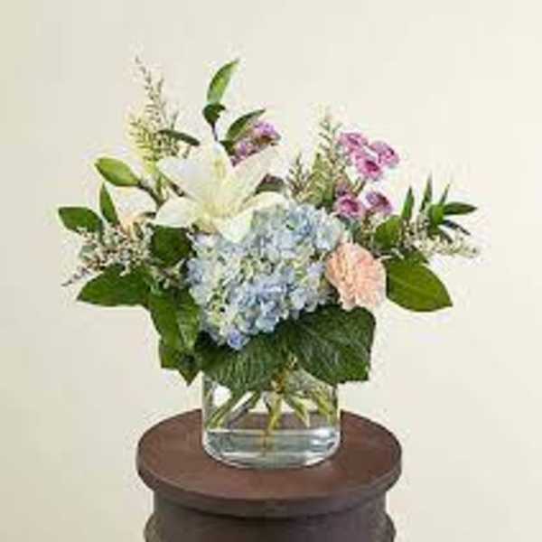 Mixed bouquet in a clear glass vase with white lily and blue hydrangea
