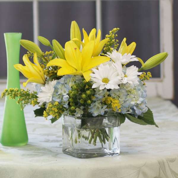 Yellow lilies and white daisies in a clear glass vase