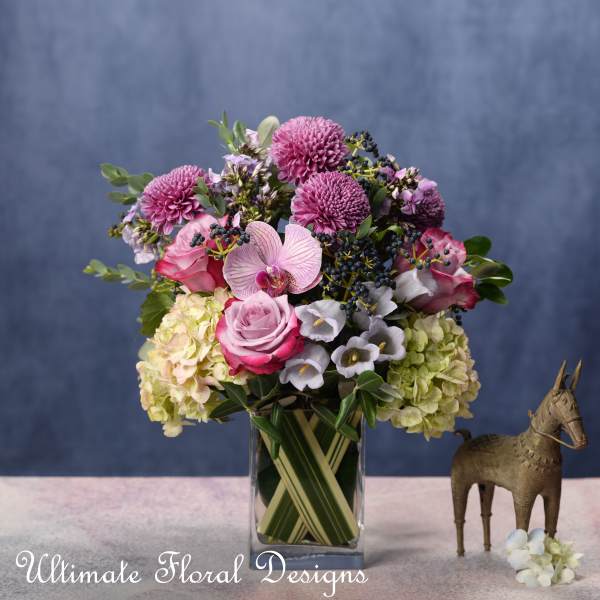 Pink and lavender floral arrangement in a clear glass vase with a small horse figurine beside it.