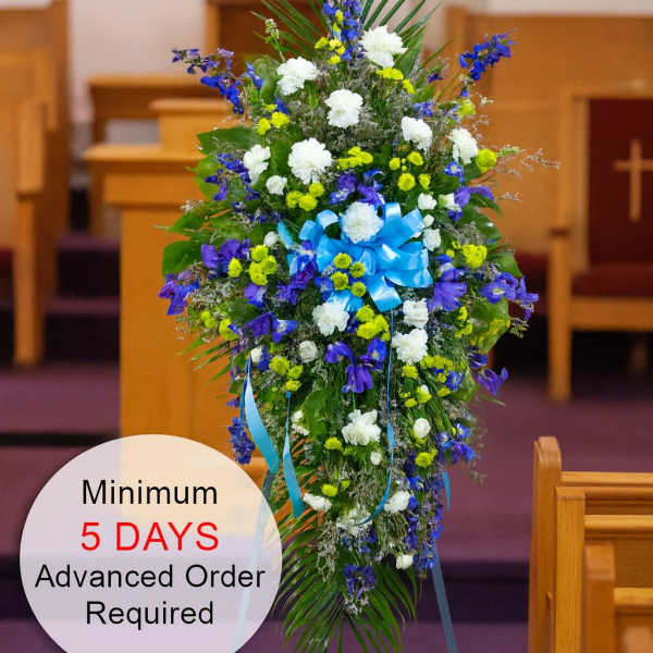 Tall blue, white, and yellow standing spray with bow on an easel in a church setting
