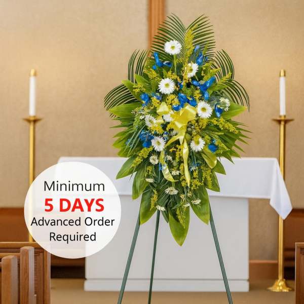 Standing funeral spray of white and blue flowers with yellow ribbon on an easel in a church sanctuary