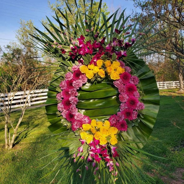 Large floral wreath with pink, yellow, and purple flowers on palm fronds