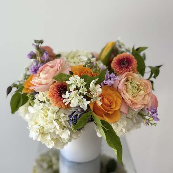 Mixed bouquet of peach, orange, white, and purple flowers in a white vase