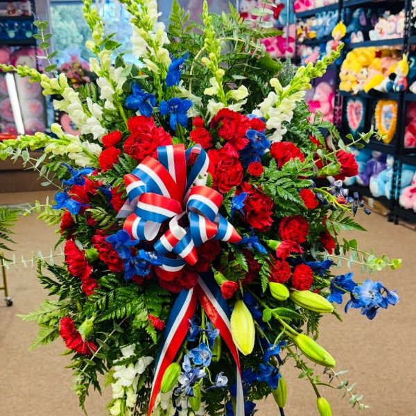 Large red, white, and blue floral standing spray with ribbon on an easel