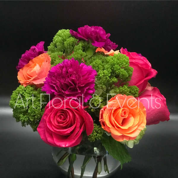 Bright pink and orange roses with purple carnations in a glass vase