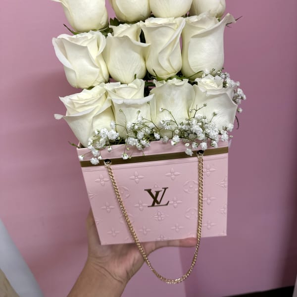 White roses arranged in a pink designer box with a gold chain handle