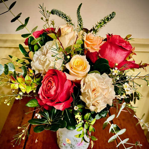 Mixed red and cream roses with peach blooms and trailing eucalyptus in a painted white vase