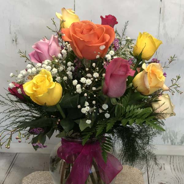 Colorful rose bouquet in a glass vase with a magenta ribbon
