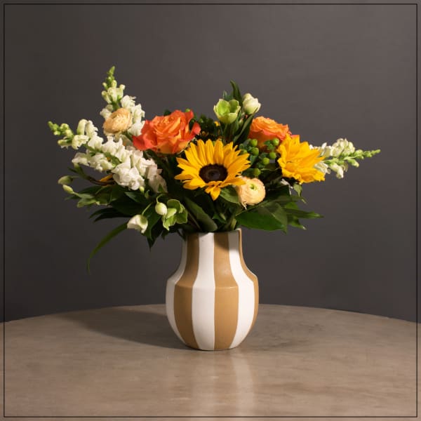 Bouquet of sunflowers, orange roses, and white snapdragons in a striped vase