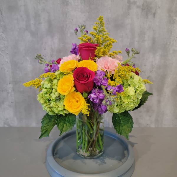 Colorful bouquet of roses, hydrangeas, and purple blooms in a glass vase