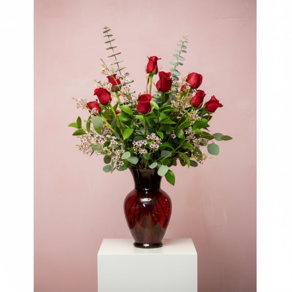 Red roses arranged in a dark glass vase with greenery