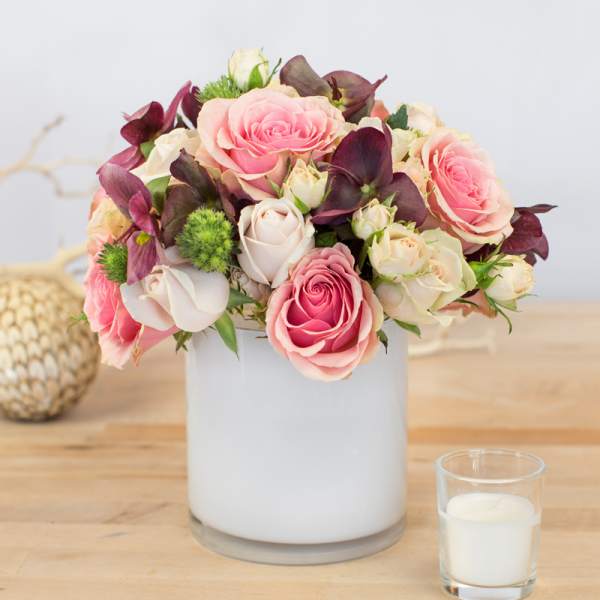 Pink and white roses arranged in a white vase with a candle nearby