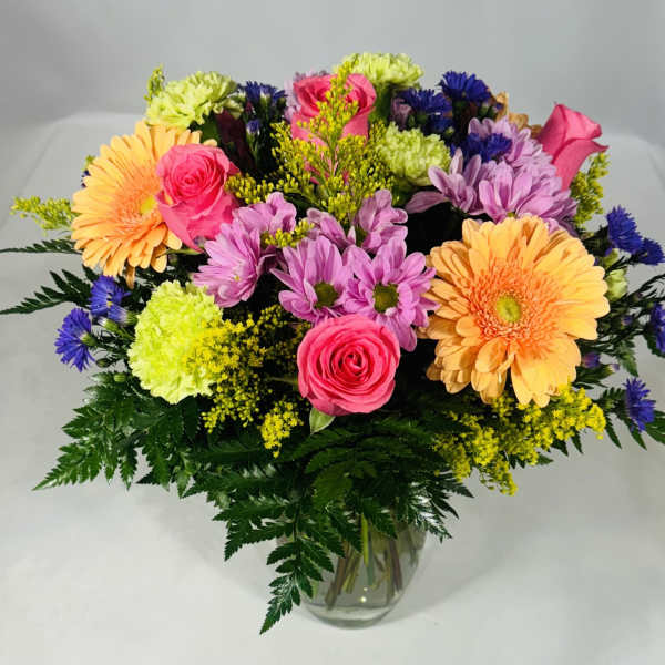 Mixed bouquet of pink, purple, yellow, and orange flowers in a glass vase