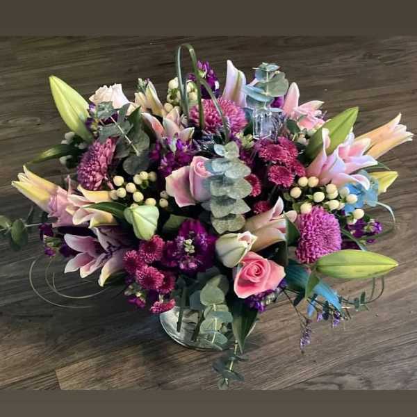 Mixed bouquet of pink lilies, roses, and purple blooms in a glass vase