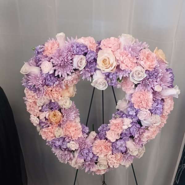 Heart-shaped floral wreath in pink, lavender, and white on a stand