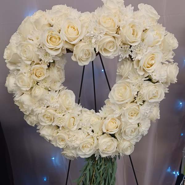 Heart-shaped white floral wreath on a stand with trailing greenery