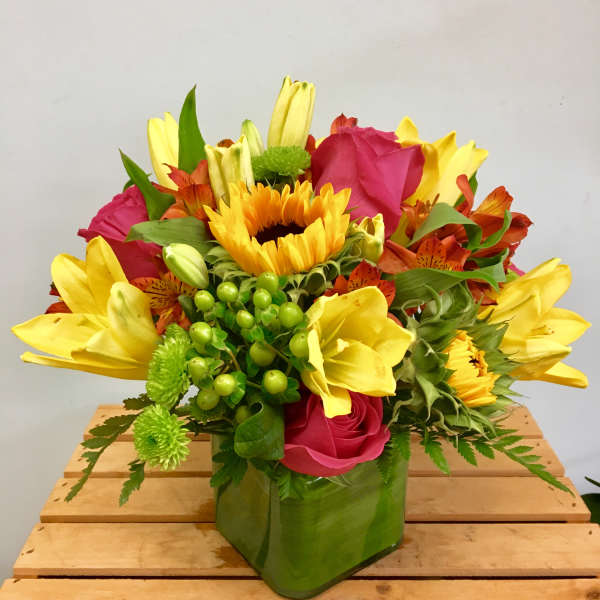 Bright mixed bouquet with sunflowers, yellow lilies, and pink roses in a green vase