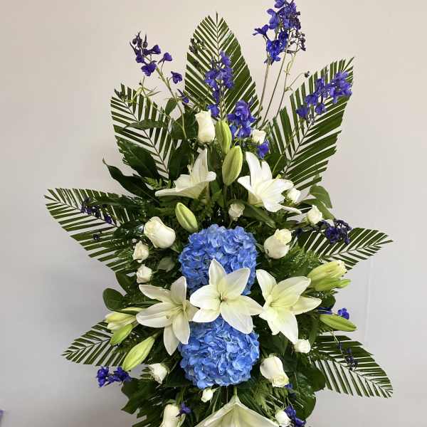 Tall floral standing spray with white lilies, blue hydrangeas, and purple flowers