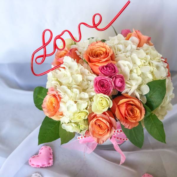 Bouquet of peach, pink, and white roses with a red wire "love" topper