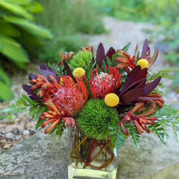 Tropical bouquet in a clear glass vase with orange and burgundy blooms
