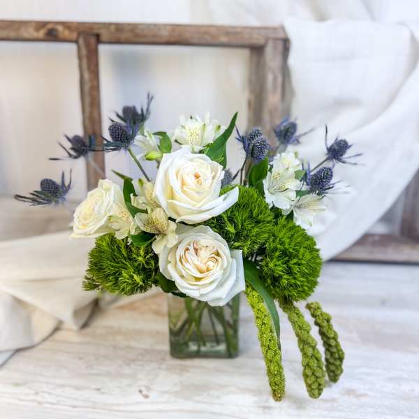 White roses and small white flowers in a glass vase with green accents
