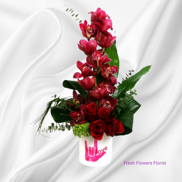 Red orchids and roses arranged in a white vase with a pink love graphic