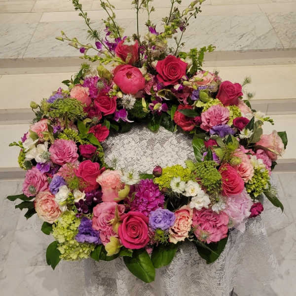 Large pink and purple floral wreath on a lace-covered stand