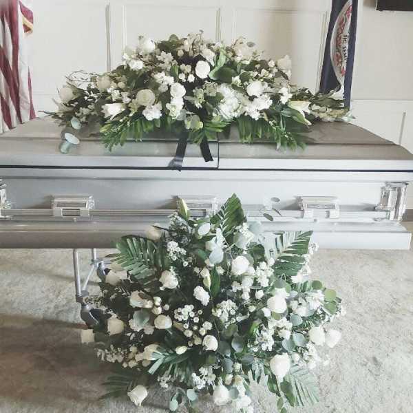 White floral sprays on a silver casket in a funeral setting