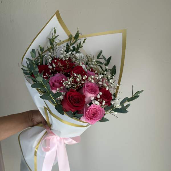 Bouquet of red and pink roses wrapped in white paper with a pink ribbon