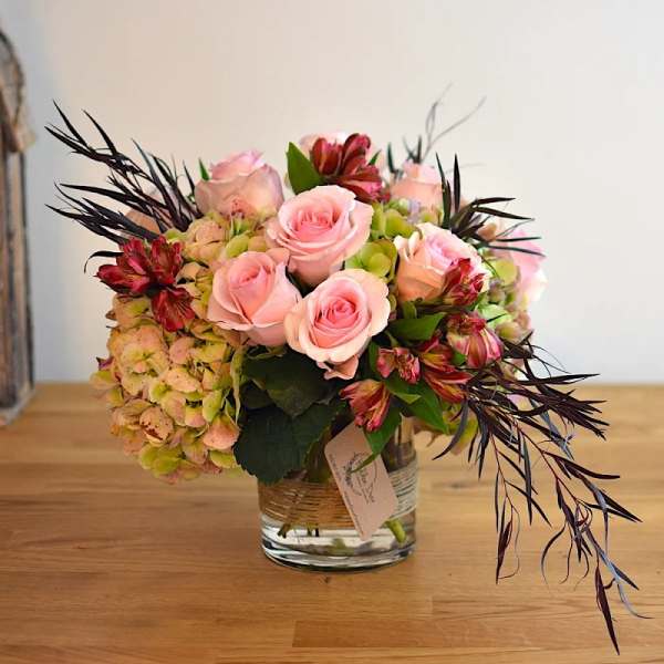 Pink roses and hydrangeas in a glass vase with dark foliage