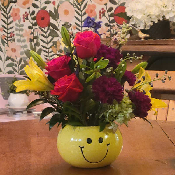 Mixed bouquet in a yellow smiley-face vase with roses and lilies