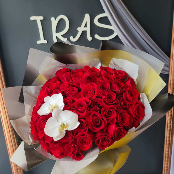 Bouquet of red roses with two white orchids wrapped in layered paper