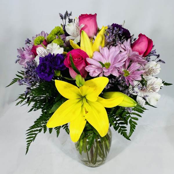 Mixed bouquet of yellow lilies, pink roses, and assorted blooms in a clear glass vase