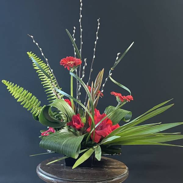Red gerbera daisies in a black container with tall willow branches
