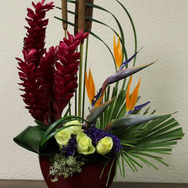 Tropical arrangement with red flowers, bird-of-paradise, and roses in a red vase