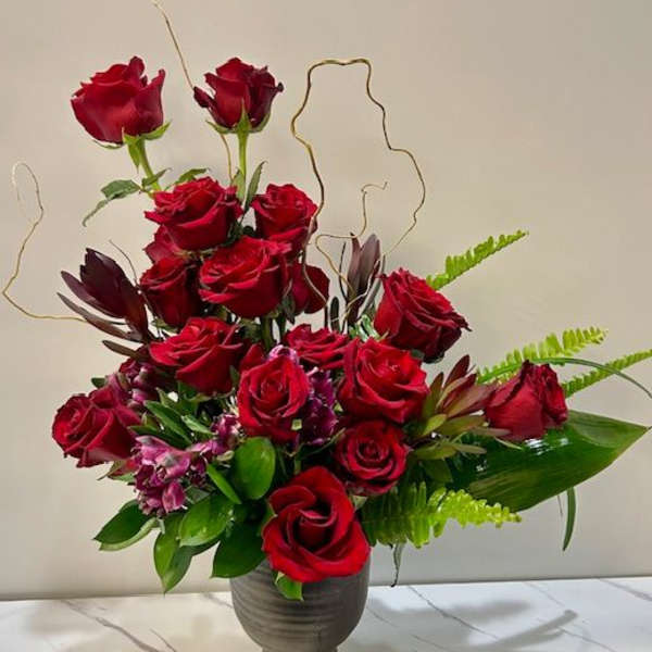 Red roses arranged in a dark vase with green foliage