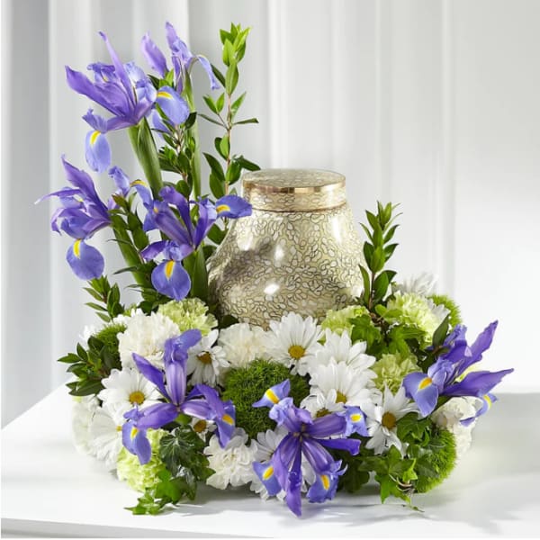 Purple irises and white daisies arranged around a decorative urn.