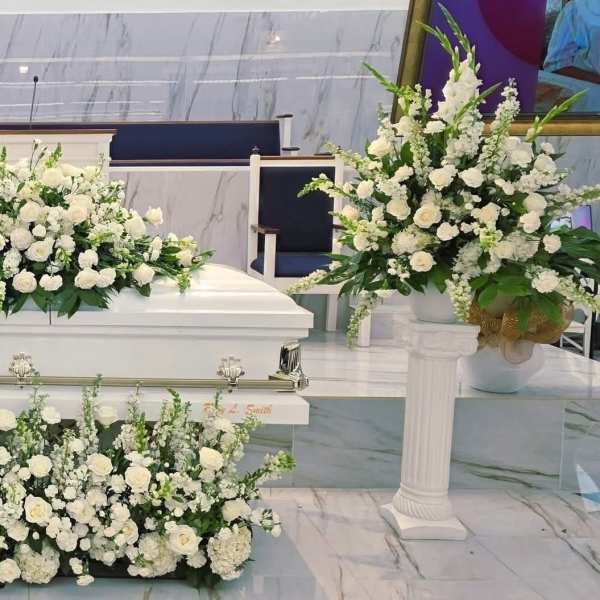 White floral funeral spray arranged around a white casket