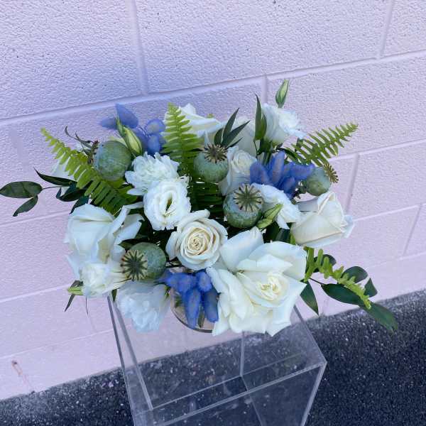 White rose bouquet with blue accents and green foliage in a clear vase