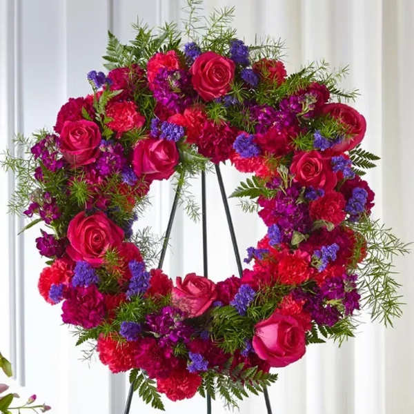 Circular floral wreath with pink roses, red carnations, and purple filler flowers