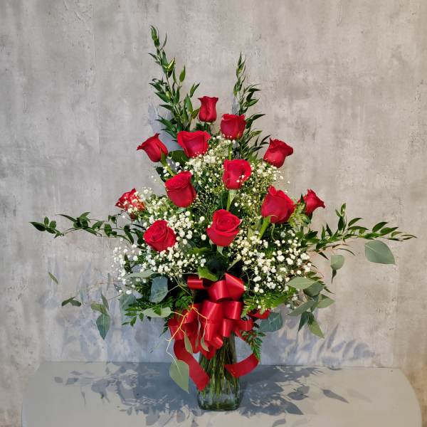 Red roses arranged in a clear glass vase with baby's breath and greenery